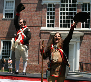 Two men dressed as Revolutionary War soldiers holding their hats up in the air in celebration.