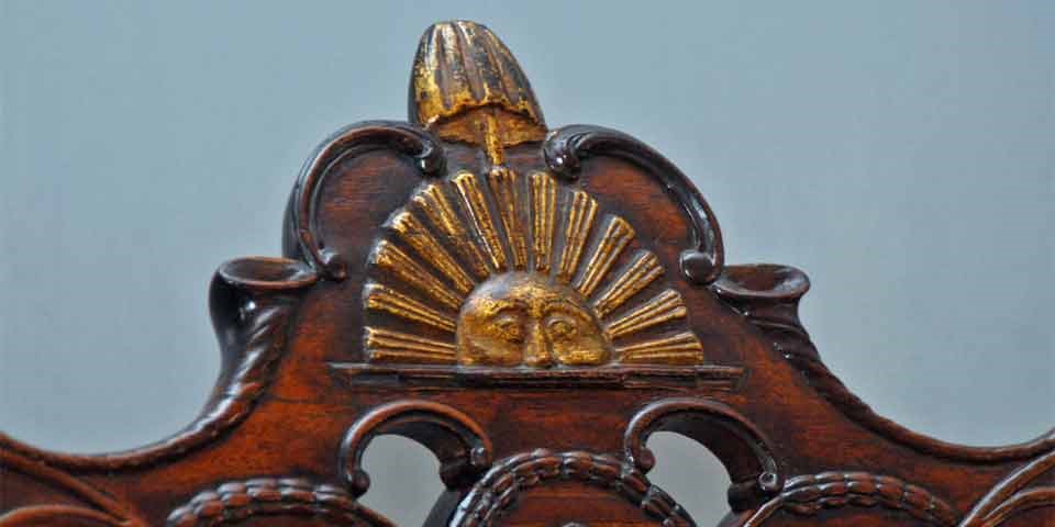Color photo showing close up of sun, liberty pole, and liberty cap carved into crest rail.