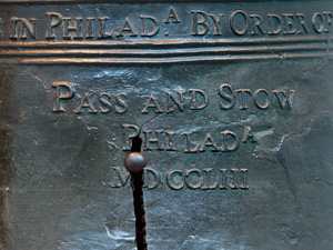 Color photo showing a detail of the Liberty Bell focusing on a thin crack growing out of a much larger crack in the "P" of "Phila" on the bell.