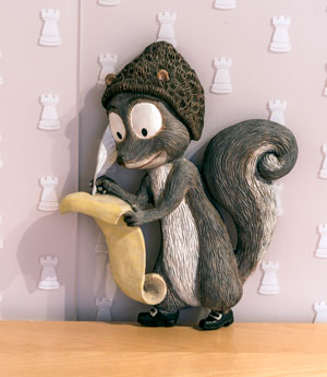 Skuggs the Squirrel figure, shown with a quill pen and scrolled paper.