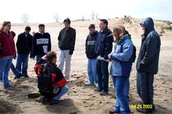 Students standing on the beach around a teacher