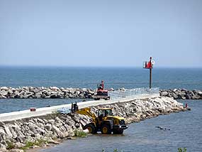 stone wall out into water with smooth walkway on top with equipment installing hand rails