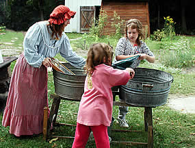a lady in 1900 cloths showing children how to use a wash tub and wringers to wash cloths