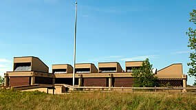 large building with tall grass in the foreground and flag pole next to building