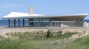 modern building with large glass walled room and curved roof with blue water of Lake Michigan in the background