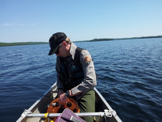 A biologist lowers an instrument in a lake from a canoe to take scientific measurements
