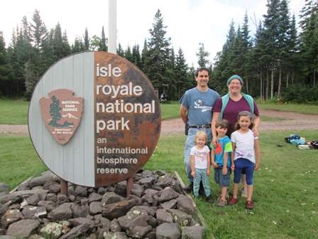 A family stands for a photo around the Isle Royale International Biosphere Sign