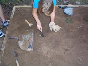 Child scraping away the dirt in the Children's Dig Box to expose artifacts