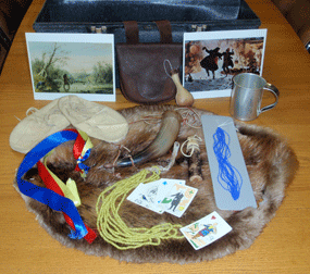 contents of Mountain Men traveling trunk: beaver pelt, trading beads and ribbons, playing cards, tobacco twist, powder horn, moccasins, tin cup, bait bottle, leather flask