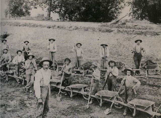 A group of workmen lined up with wheel barrels and shovels.