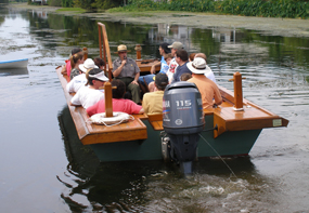 A ranger and several people on a wooden boat enjoy a tour on a bayou near the Wetlands Acadian Cultural Center