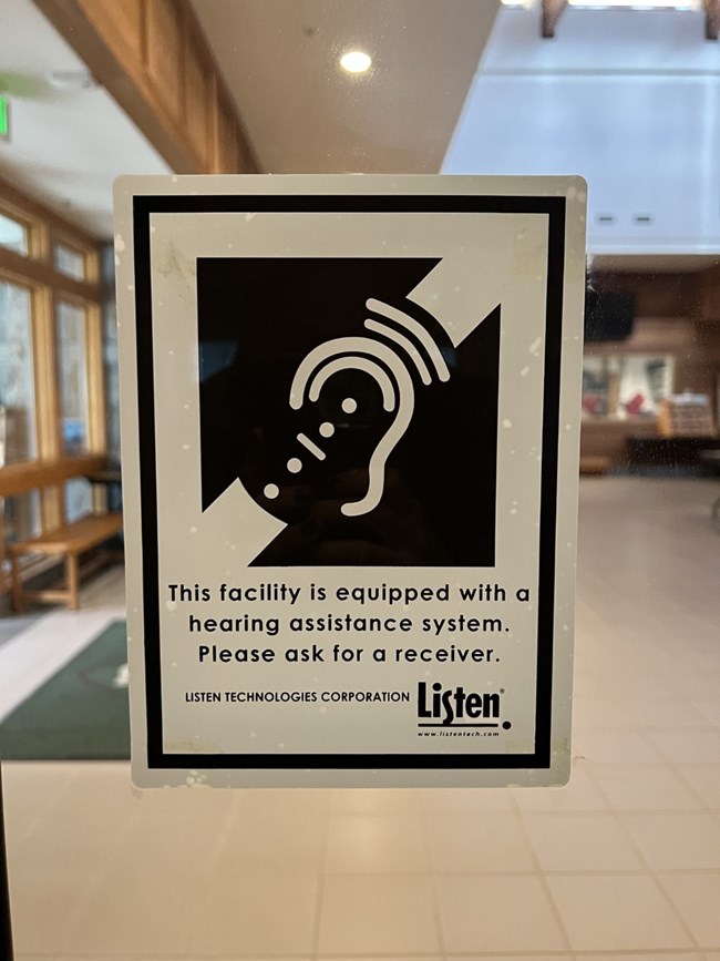 A sign with text, "This facility is equipped with a hearing assistance system. Please ask for a receiver."