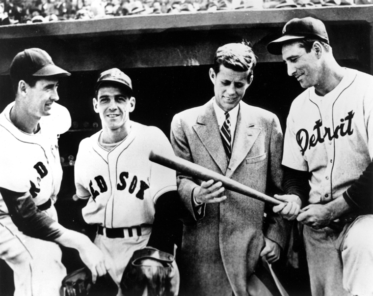 John F. Kennedy holds a baseball bat while talking to Boston Red Sox players.