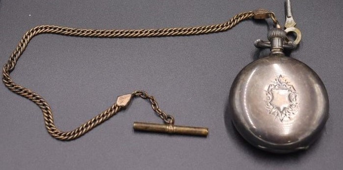 A 19th century metal and glass pocket watch with a chain and key attached. It was gifted to Johnstown Flood National Memorial in 1991.