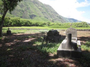 A cement grave site and marker in a field that is Kahaloko Cemetery