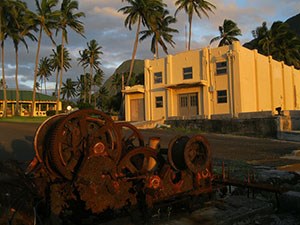 A large building and rusty gear in front of it.