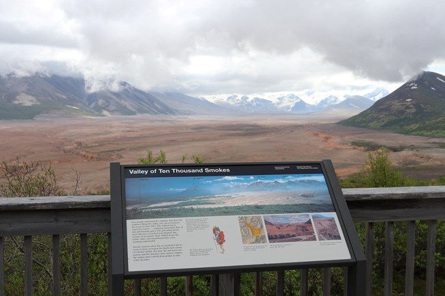 Interpretive sign in the foreground with ashen valley and mountain landscape in background.