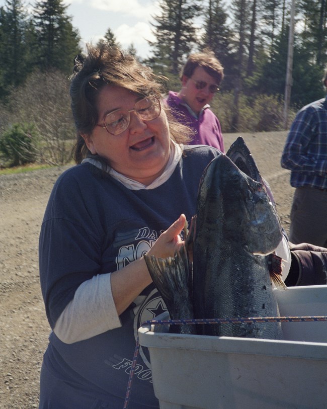 A woman pulls a salmon out of a tote.