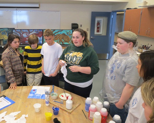 Art students stand around a table while a guest artist teaches them the techniques for their projects.
