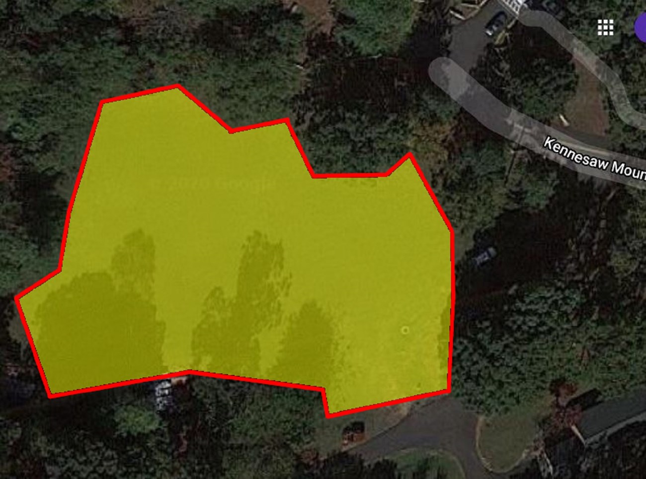 Yellow highlights jagged field area surrounded by trees. Right side of field has narrow asphalt path ways and top right section shows the end of Kennesaw Mountain Rd.