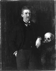 Man dressed in a suit rests his elbow against a table with a human skull on it. He has short, bushy, gray hair and a bushy mustache the width of his mouth.