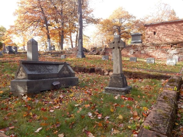 Grave markers are surrounded by a small, masonry fence in a cemetery.