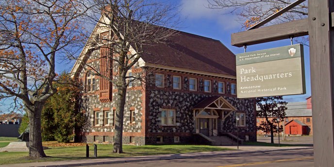 The Keweenaw History Center building in the background, with the park headquarters sign in the foreground.