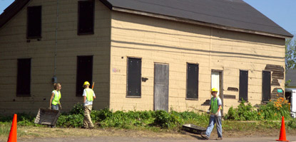 Members of the park Youth Conservation Corps clean around the outside of a Quincy company house.