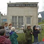 A female ranger holds a photograph with a historical photo to compare with historic building behind her.