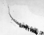 long chain of people ascend snowy slope