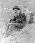 elderly, bearded man sits with pack on back