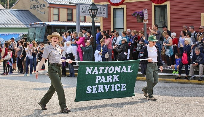 Two people carrying "National Park Service" banner on a crowded street