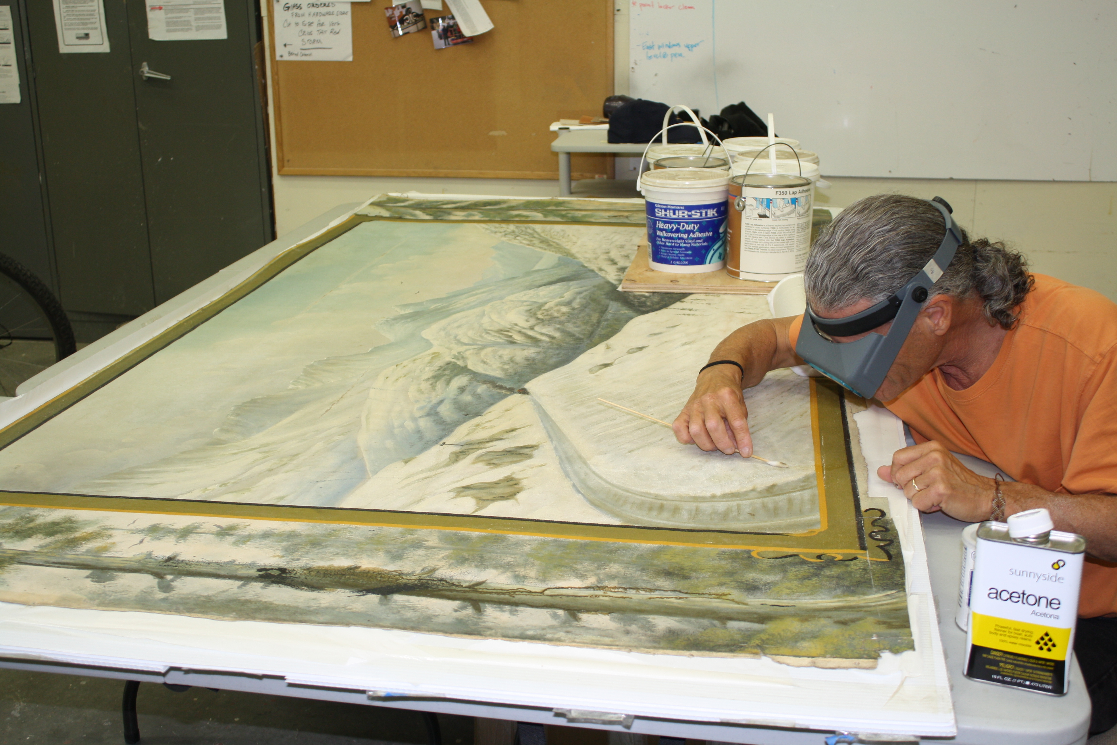 A man works on a painting with cleaning tools.