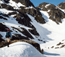  hikers walking on snow with rock cliffs and slopes above them
