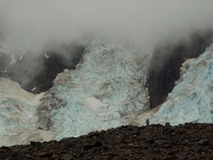 A person stands on rocky ground in front of a cascade of glacier ice