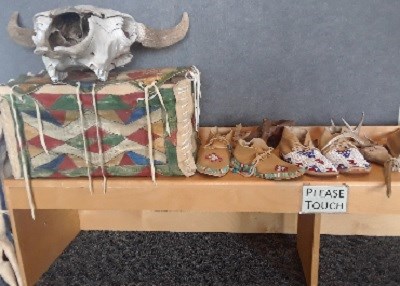 Bison skull, painted box, and moccasins displayed on a bench that reads please touch.