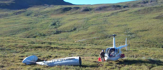 Image of hilly tundra and a helicopter preparing to remove an abandoned fuel pod