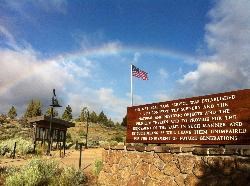 A rainbow over an American flag on a sign at the Lava Beds Visitor Center