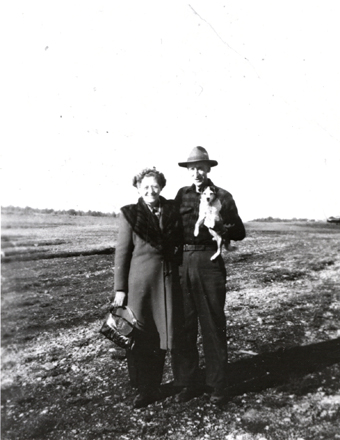 black and white image of a man and woman posing in a field, holding a small dog