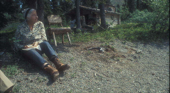 a woman and man sitting near a log cabin