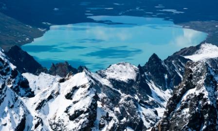 Craggy snow covered peaks in the foreground above a bright turquoise lake in the background.