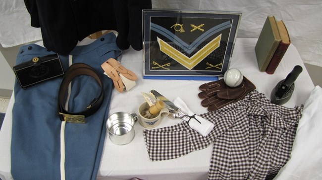 Trunk contents shown, including military uniform jacket and pants, patches, a baseball and glove, a child's smock, and other small items.