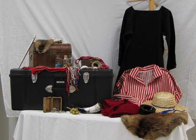 Trunk contents shown, including clothes, a beaver fur, a curved horn, a leather box, bells, and other small items for trading.