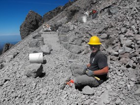 A trail crew member prepares to place a stone on a steep switchback