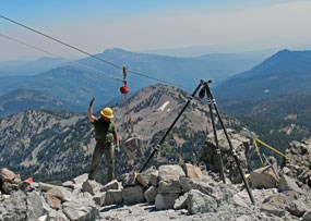 A trail worker guides a boulder on a pulley system