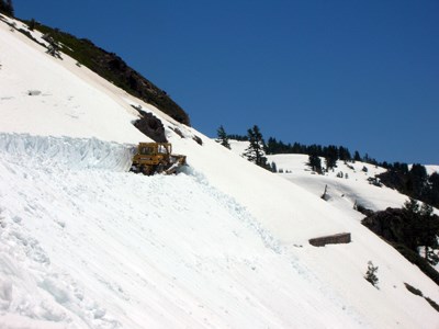 A bulldozer pushes deep snow off a slope below Emerald Lake on the park highway.