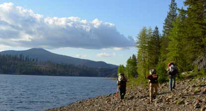 Backpackers walk along the rocky shore of Snag Lake