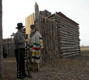 Reenactors in period clothing stand outside a replica of Camp Dubois, a log fort.
