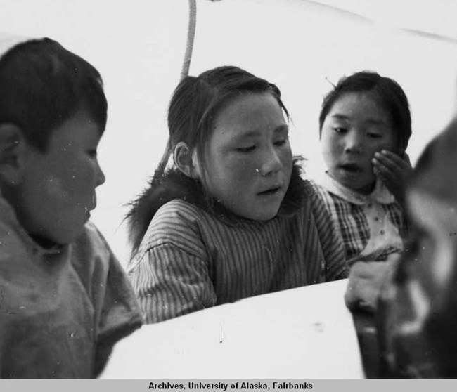 three schoolchildren, one boy and two girls, look together at a paper.