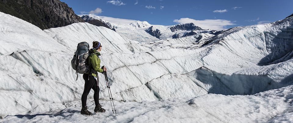 a woman stands with a pack on root glacier